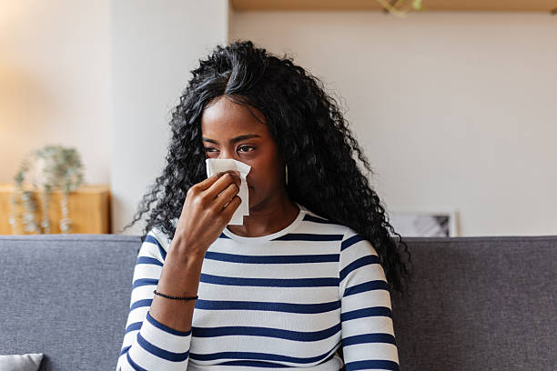 istock Sick black woman blowing nose while sitting on sofa at home 2253312466