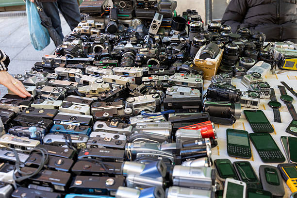 Madrid, spain; 11 15 2025 hand browsing many old film cameras, lenses, and electronics at a market in madrid