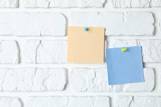 istock Colored paper stickers attached with pushpin on a white brick wall 2253314404