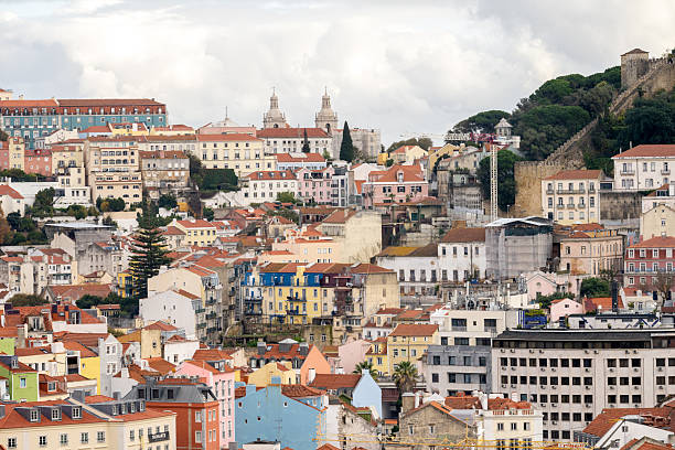 Lisbon Portugal December 06 2025. Colorful residential buildings fill the Alfama hillside with Sao Jorge Castle walls and a construction crane above.