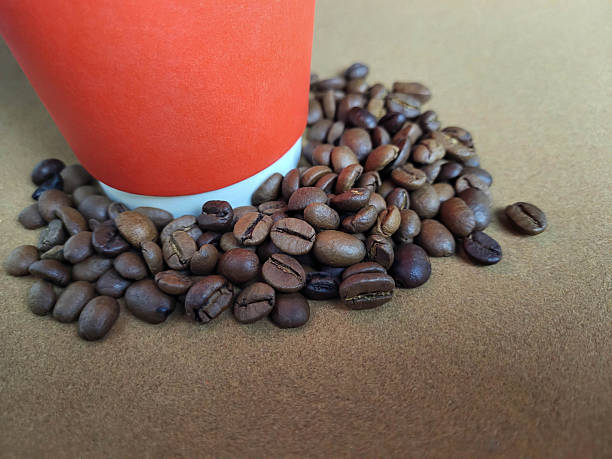 A part of a red paper cup with scattered coffee beans on a brown background