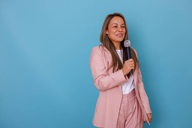 istock Woman speaker holding microphone, giving presentation or public speech on light blue background 2253320097