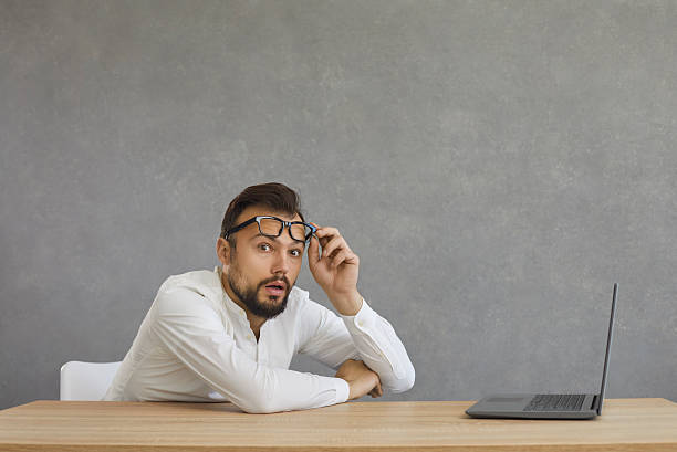 istock Man sitting at desk with laptop and looking at camera with shocked face expression 2253320238