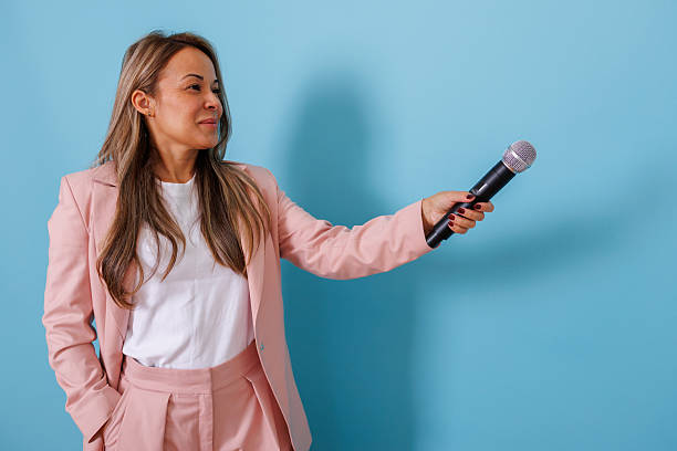 istock Woman in pink suit jacket holding a microphone, looking away, ready for an interview or reporting news 2253321704