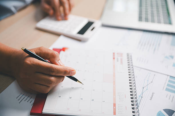 istock Office worker marking calendar while calculating financial data, illustrating schedule planning, time management, business tasks, productivity, professional workflow in modern workplace environment. 2253330628