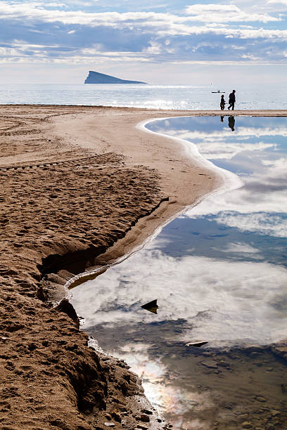 Sandwich, Massachusetts, USA- September 4, 2025-  Two middle aged people are reflected in the wet sand as they stop along the edge of a beach for a brief conversation  at the water's edge.
