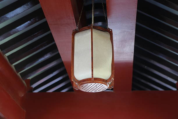 a hanging lantern with an open square white felt cover and red leather edges hangs from the ceiling on one side, with black strips on both sides. the interior is dark brown or light gray.