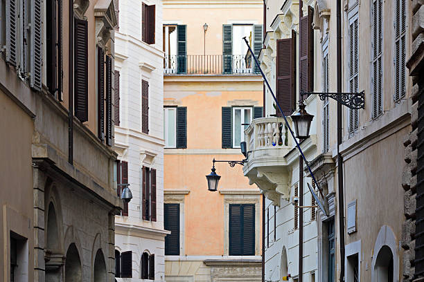 Building facades with shuttered windows along a narrow street in Rome, Lazio, Italy. The historic urban architecture reflects traditional building design within the Italian capital.