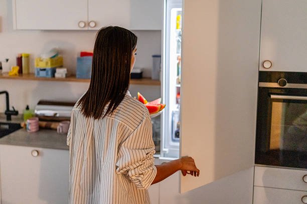 istock Young woman stands in kitchen at home looking inside open refrigerator during the weekend 2253345173