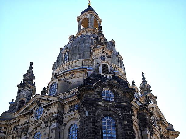 A striking close-up view of a baroque church dome showcasing intricate stone details and arched windows in Dresden. The historic structure stands out against a clear, bright sky. Ideal for themes of European architecture, culture, heritage, and travel.