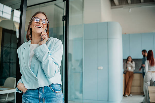 istock Employee smiles while talking on the phone in a bright office setting during working hours with colleagues engaged in conversations nearby 2253347960
