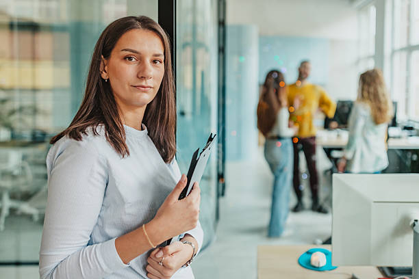 istock Group of adults engaged in work and discussions in a modern office setting while one person holds a clipboard 2253348305