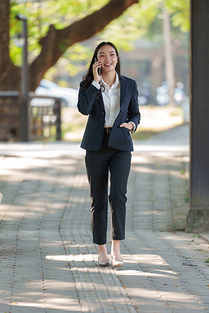 istock Confident businesswoman in a professional suit walking along a tree-lined path while engaging in a phone conversation, embodying modern communication and professionalism 2253351091