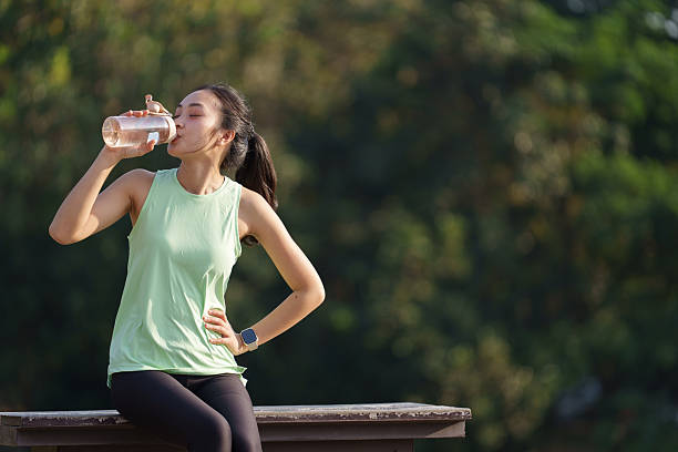 istock Woman in athletic wear drinking water outdoors, taking a break from exercise. The lush greenery in the background suggests a natural, refreshing environment for physical activity 2253352922