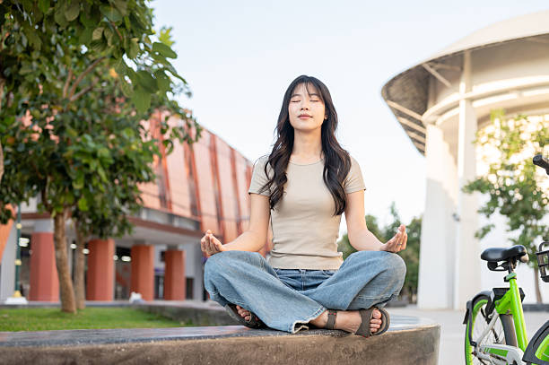istock Pretty asian woman closing eyes meditating while sitting folding legs on bench aside bicycle in park 2253353113
