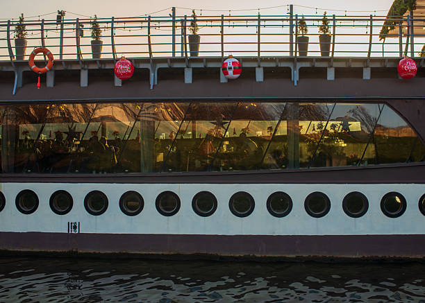 Krakow, Poland – December 13, 2025: A floating restaurant moored on the Vistula River is decorated with Christmas ornaments and lights, with silhouettes of guests visible through large windows during the winter season.