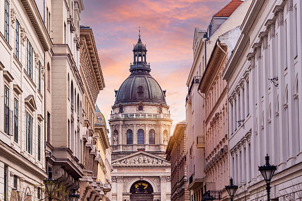 Scenic view of St. Stephen's Basilica framed by historic buildings in Budapest, Hungary during a colorful sunset sky.