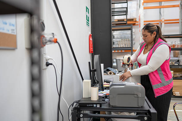 A female warehouse employee stands and tapes a package at a dispatch desk