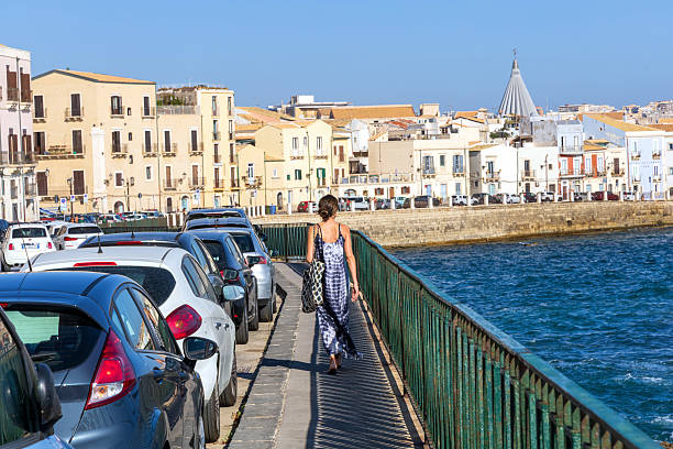 Young woman walking along Syracuse sunny waterfront. Syracuse, Italy - October 10, 2025