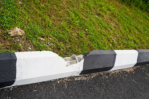 Damaged black and white painted curb separating asphalt road from a grassy embankment.