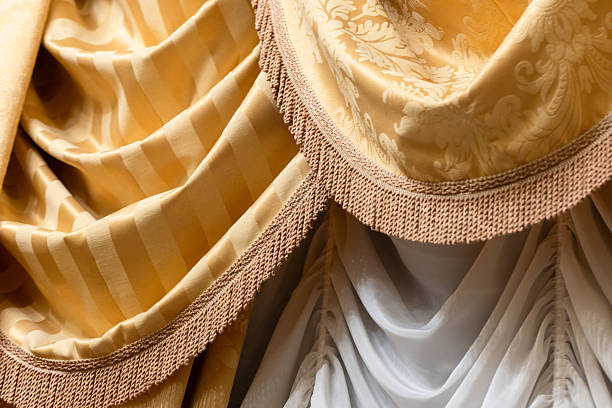 Elegant gold fabrics featuring striped and damask patterns, layered with fringe trim. Perfect for upscale decor, curtains or background textures. Warm tones evoke luxury, comfort and refined interiors