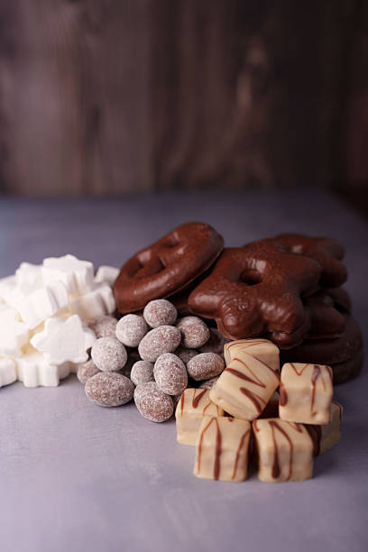 assorted holiday cookies and confections on textured surface with dark wooden background, featuring chocolates, sugar-coated delights, marshmallow shapes, and baked goods, delight, decor, crisp