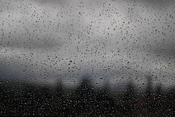 Water droplets on a glass surface with a cloudy gray sky in the background. A simple yet emotional representation of rainy weather and calm introspection.