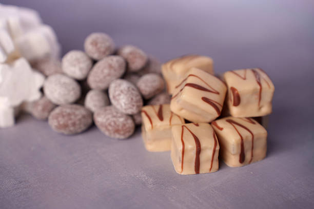 close-up of assorted confections featuring fudge cubes with chocolate drizzle and sugar-coated almonds on soft lavender surface with gentle lighting, elegant, palette, presentation, visual