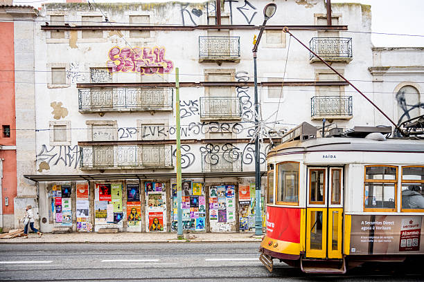 Lisbon Portugal December 06 2025. A yellow tram passes residential buildings with graffiti balconies and street posters in Bairro Alto.