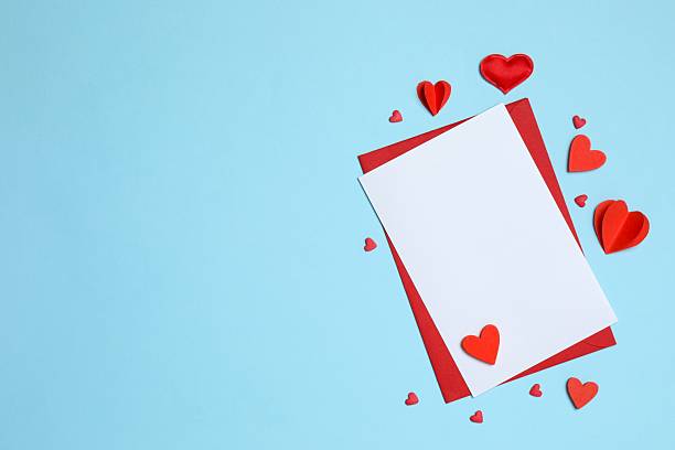 istock Red paper envelope with blank white note mockup inside and Valentines hearts on blue background. Flat lay, top view. Romantic love letter for Valentine's day concept. 2253369980