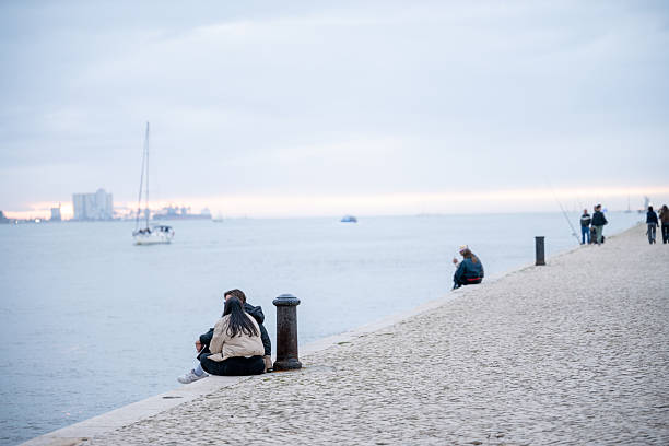 Lisbon Portugal December 06 2025. People sit and walk along a riverside promenade beside the Tagus River during an overcast afternoon.