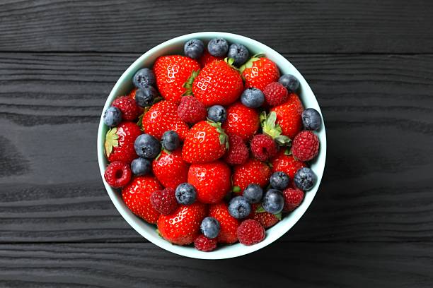 istock Different fresh ripe berries in bowl on wooden table, top view 2253370623