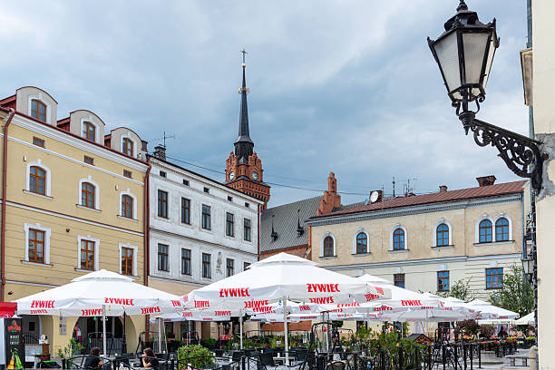 Tarnow, Poland – July 12, 2025: Outdoor restaurant tables with large umbrellas occupy a historic town square, surrounded by classic architecture and summer greenery under calm daylight conditions.
