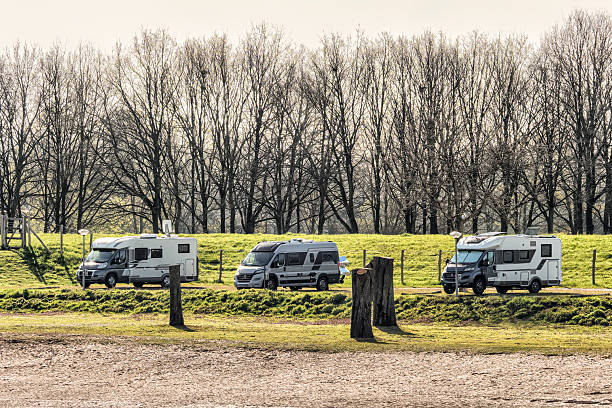 Three RVs parked on green grass in Lathum, Gelderland, Netherlands, with bare trees in background