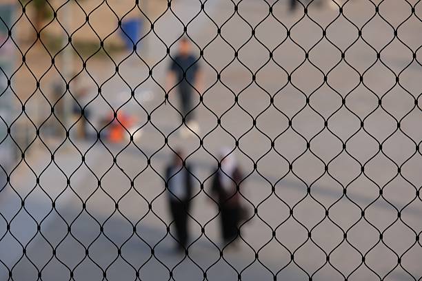 A blurred view of two people standing behind a fence, with an out-of-focus background showing a street scene