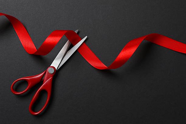 istock Scissors cutting red ribbon isolated on black surface 2253377312