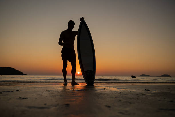 Silhouette young man entering the ocean at sunset while holding surfboard expressing freedom and an adventurous beach lifestyle outdoor sports personal growth and inspirational summer lifestyle.