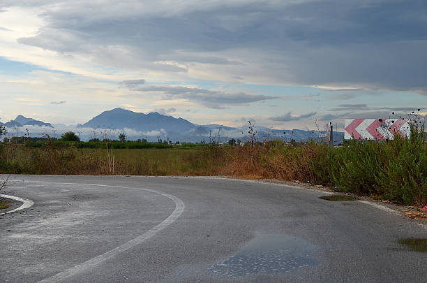 Empty asphalt road with a central white line extending into the distance, bordered by a guardrail and trees, under a bright blue sky