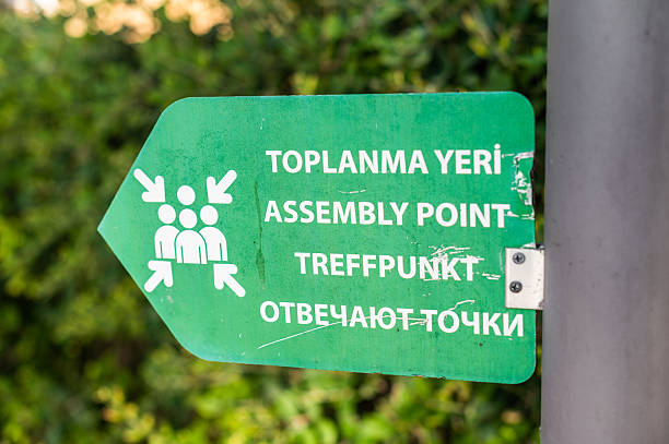 istock Sign indicating assembly point in multiple languages located in a green area during daytime 2253380663