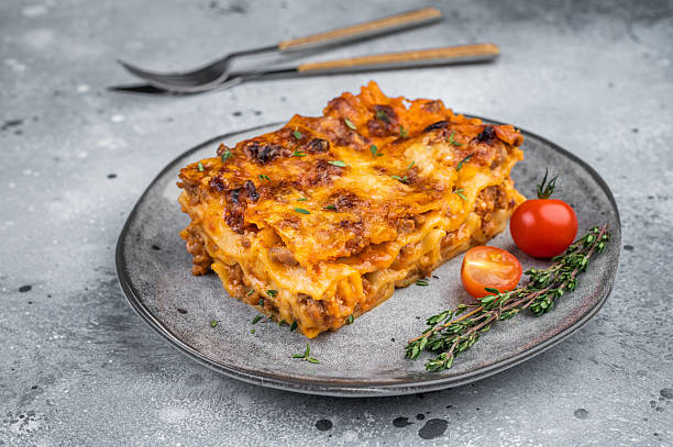 istock Homemade beef lasagna portion with baked cheese thyme garnish and cherry tomatoes on light stone background 2253381999
