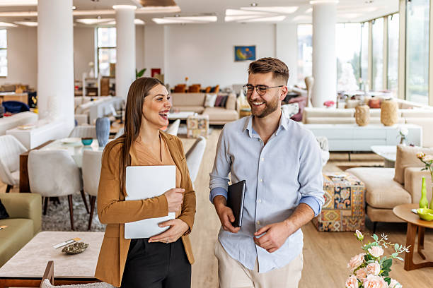 istock Friendly Professionals In A Modern Furniture Store Share A Smile While Carrying Laptops 2253383616