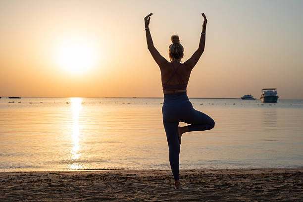 istock Woman is performing tree pose balancing on one leg, celebrating wellness and tranquility during sunrise on a sandy beach. 2253385290