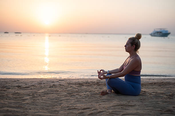 istock Woman is meditating on beach during sunrise with ocean. 2253385316