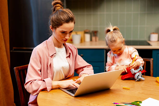 istock Mother working from home on laptop while daughter playing in kitchen apartment 2253388486
