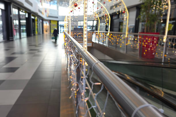 Sunlit empty hallway in a modern shopping mall with clean white tile floor, tall pillars, glass wall, indoor potted palms in metal planters, reflections and long perspective creating a minimalist architectural background with ample copy space for retail, airport, hospital or office concepts