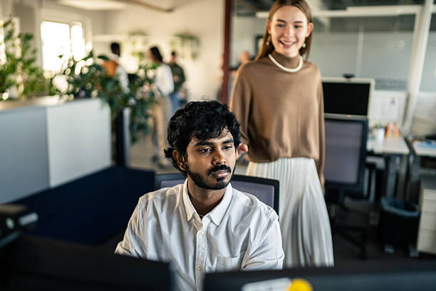 istock Smiling Colleague Approaching a Coworker at His Desk 2253392709