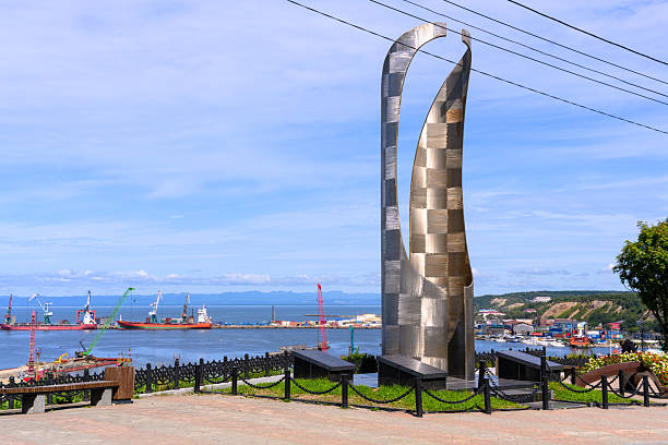 Korsakov, Russia - August 30, 2025: A stunning metal sculpture rises above the harbor, framed by boats and a captivating blue sky. The scene captures a lively atmosphere and artistic beauty near the water.