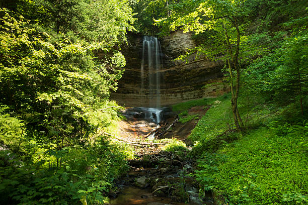 Photo of Alger Falls cascading down layered rock near Pictured Rocks National Lakeshore in Michigan with roadside view and natural surroundings.