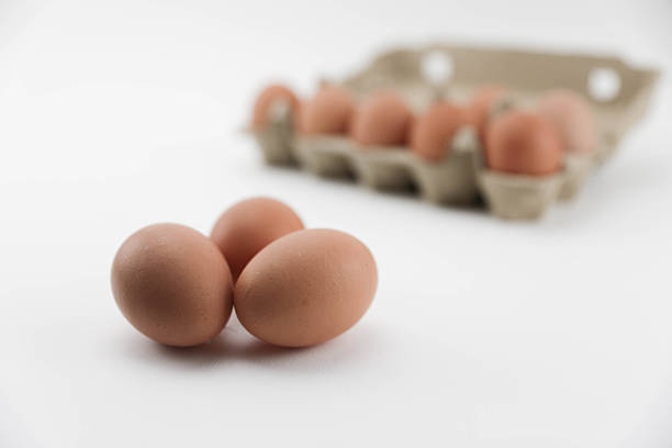 Brown eggs arranged around an open carton on a white background, showcasing natural farm-fresh produce in a clean, minimal studio setting.