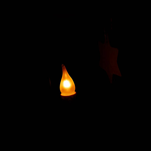 LED candle flame casts a star silhouette on a dark background, providing soft, warm light